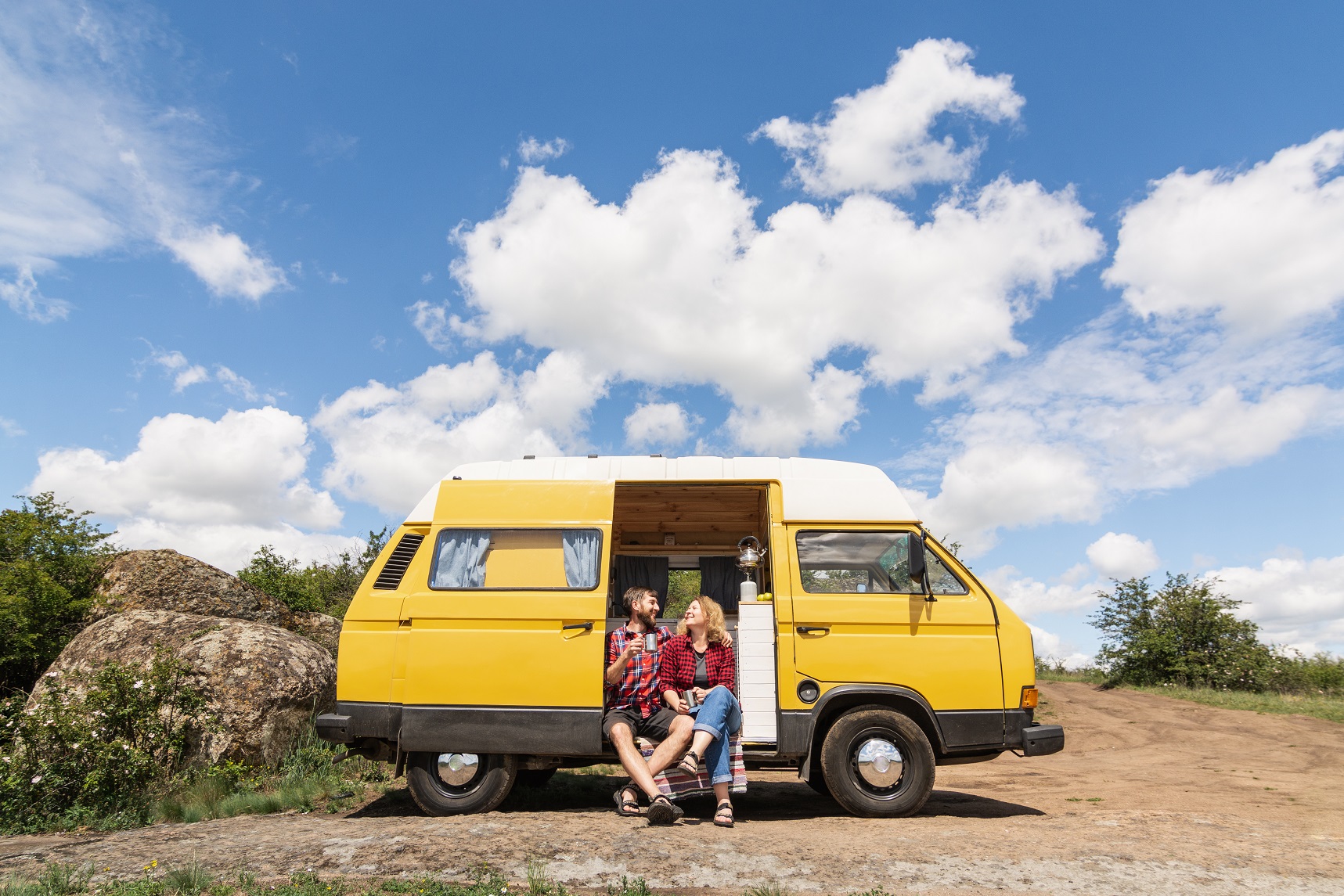 Young Eastern European couple travelling by yellow camper van though the countryside. Self built off-grid motorhome camping in the wild nature.